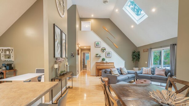 Um amplo loft com área de refeições, cozinha e sala de estar. É visível um claraboia e uma escada.