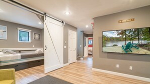 Um quarto com porta deslizante, uma cama, uma cadeira e um quadro com uma paisagem de lago.
