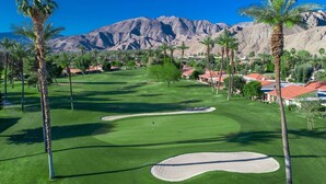A golf course with palm trees, a sand bunker, and a mountain backdrop. - Spectacular view, steps to pool/jacuzzi at Sunrise Country Club-winter available (Rancho Mirage)