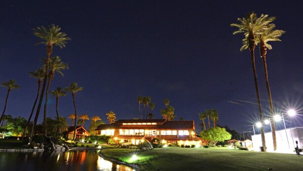 A large, illuminated hotel with multiple floors, a swimming pool, and tall palm trees. - Spectacular view, steps to pool/jacuzzi at Sunrise Country Club-winter available (Rancho Mirage)