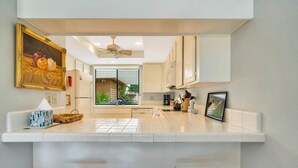 A modern kitchen with white cabinets, a central island, and a ceiling fan. - Spectacular view, steps to pool/jacuzzi at Sunrise Country Club-winter available (Rancho Mirage)
