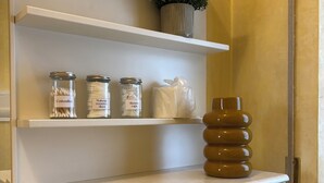 Um banheiro com armários brancos, uma prateleira com cotonetes, discos demaquilantes e toucas de banho, e uma planta em vaso.