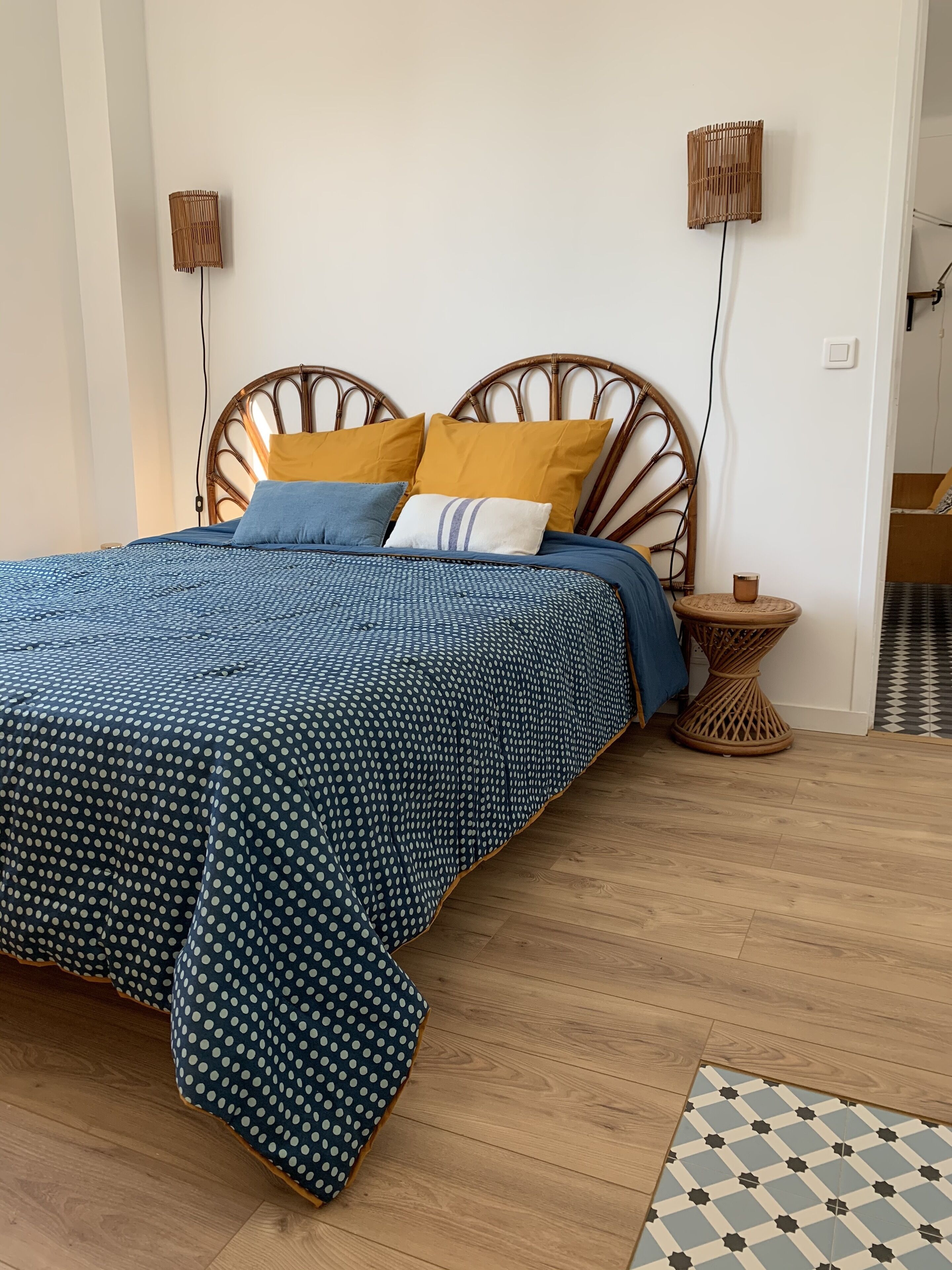 Una cama con edredón de lunares, cabecera de madera y dos lámparas de noche.