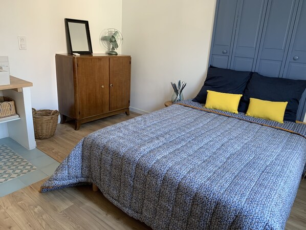 Un dormitorio con una cama, un armario de madera, una mesita y una cesta de mimbre.