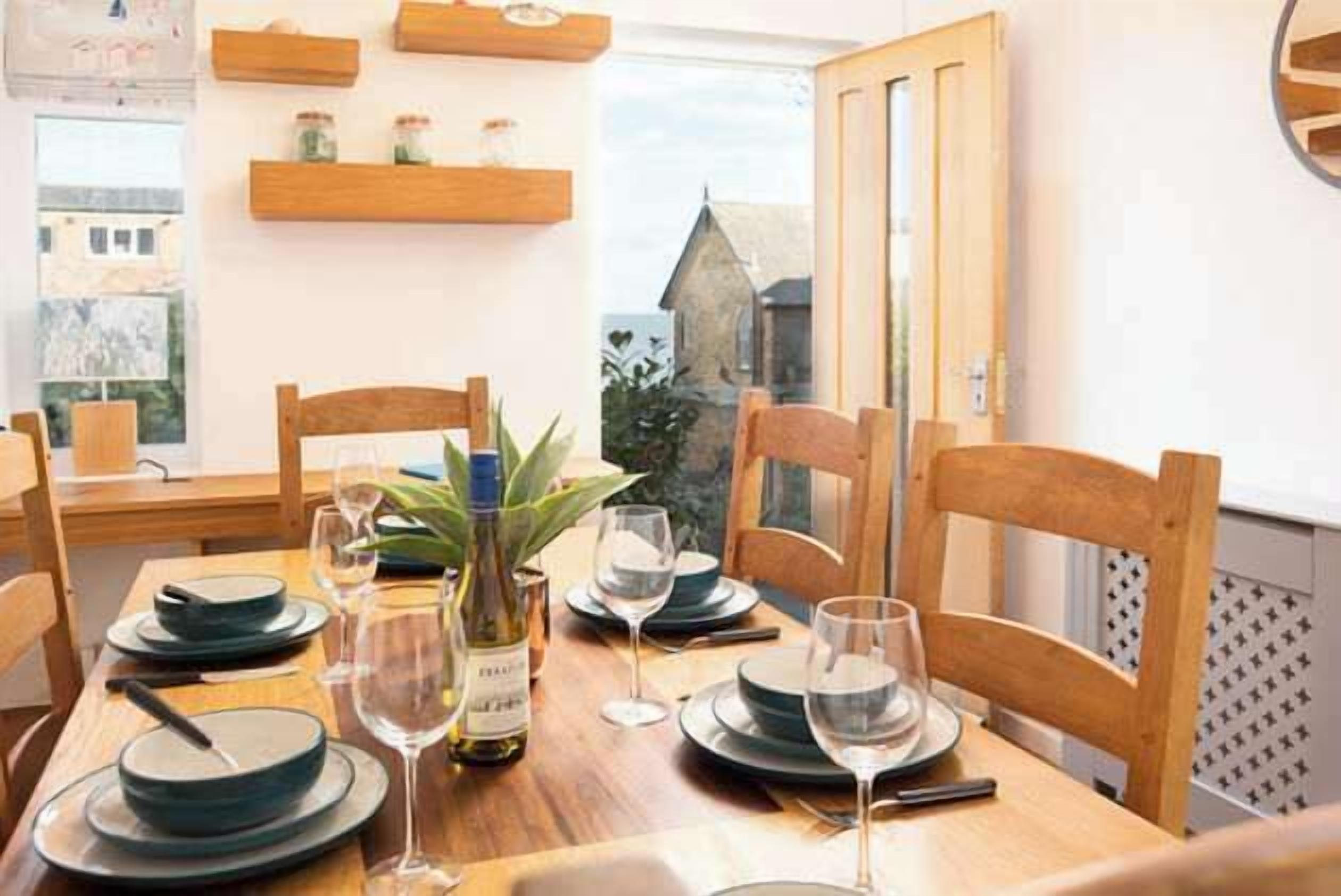 Une table à manger dressée avec des assiettes, des verres et une bouteille, entourée de chaises en bois.
