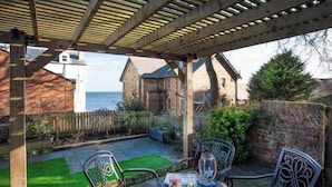 Une terrasse couverte avec une table et des chaises, une vue sur la mer et un bâtiment en pierre en arrière-plan.