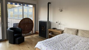 Un dormitorio con cama, una silla, una mesita de noche de madera, un calefactor y una puerta corrediza de cristal que da a un balcón.