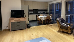 Una sala de estar moderna con televisor, muebles de madera, una mesa de comedor y un sillón de cuero.