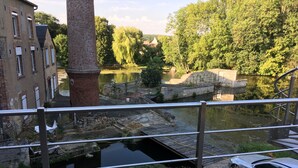 Vista al río desde un balcón con barandilla de metal, un edificio de ladrillo y un puente.