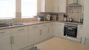 A kitchen with white cabinets, a sink, a stove, and a window with blinds. - Jubilee House  - 4 bedroom central house - bright and spacious, 2 parking space (Filey)