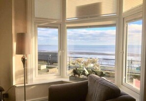 A room with a large bay window overlooking a coastal view, a floor lamp, and a sofa. - Ivy House - Seafront house with garden seating and stunning sea views! (Filey)