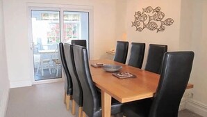 Un coin repas avec une table en bois et des chaises noires, un élément décoratif mural et une vue à travers une porte vitrée.