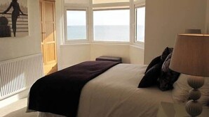Une chambre avec un grand lit, une vue sur la mer par la fenêtre, un radiateur et une lampe.