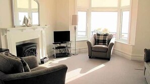 Un salon avec une cheminée, un téléviseur et deux fauteuils.