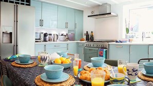 A modern kitchen with light blue cabinets, stainless steel appliances, and a dining area set with blue and white dishes, orange juice, and pastries. - Flora Dora - Luxury cottage, central, beautiful (Filey)