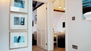 A hallway with framed abstract art, a white door leading to a bedroom with a bed and a TV, and pendant lights. - Flora Dora - Luxury cottage, central, beautiful (Filey)
