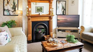A living room with a fireplace, a television, and a coffee table with books and a plant. - Glenview House - Fantastic child friendly house - rear garden - parking (Filey)