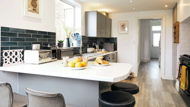 A modern kitchen with a central island, black tiled backsplash, stainless steel appliances, and a view into the dining area. - Glenview House - Fantastic child friendly house - rear garden - parking (Filey)