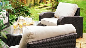 A wicker outdoor seating area with a table set for a meal, surrounded by greenery and a wooden fence. - Glenview House - Fantastic child friendly house - rear garden - parking (Filey)