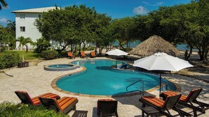 A pool with lounge chairs and umbrellas, surrounded by trees and a building.