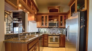 A kitchen with wooden cabinets, stainless steel appliances, a tiled backsplash, and a built-in bookshelf.
