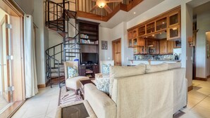 A living room with a sofa, a television, a bookshelf, a staircase, and wooden cabinets.