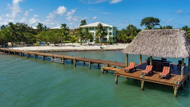 A wooden pier leading to a thatched-roof structure with lounge chairs.