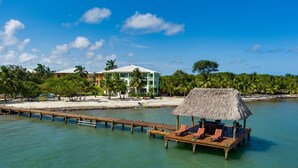 A resort with a thatched-roof hut, wooden deck, and a building with balconies overlooking the water.
