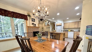 A dining area with a wooden table and chairs, a chandelier, a fireplace, and a kitchen in the background. -  Experience Vermont’s Fall Magic at here at the Lemondrop (Dover)