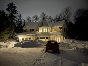 Une grande maison recouverte de neige, avec une voiture garée devant.