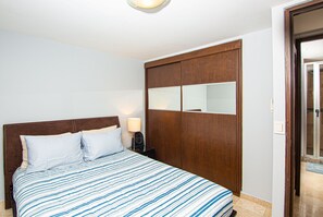 A bedroom with a bed, a nightstand, a wooden wardrobe, and a mirror.