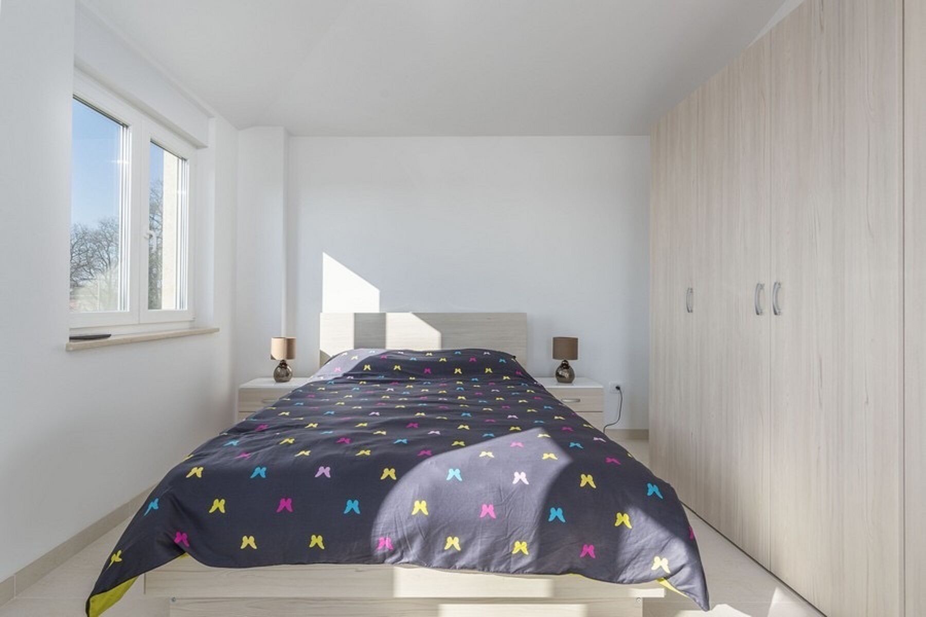 A bedroom with a bed, two bedside tables, a wardrobe, and a window.