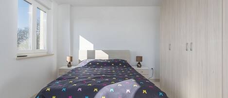 A bedroom with a bed, two bedside tables, a wardrobe, and a window.