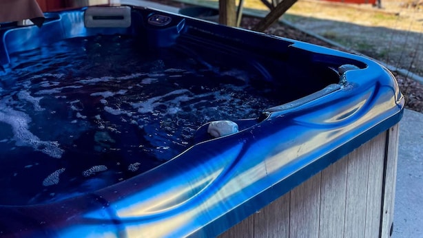A hot tub under a wooden deck with a metal roof, surrounded by a fenced outdoor area. - Presidential Barndominium at the Stable at Bear Mountain (Eureka Springs)