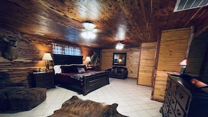 A room with a wooden ceiling, a bed, a sofa, a TV, a dresser, and a large fur rug. - Presidential Barndominium at the Stable at Bear Mountain (Eureka Springs)
