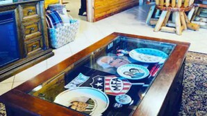 A room with a glass-top coffee table displaying various items, wooden walls, an American flag, and a television. - Presidential Barndominium at the Stable at Bear Mountain (Eureka Springs)