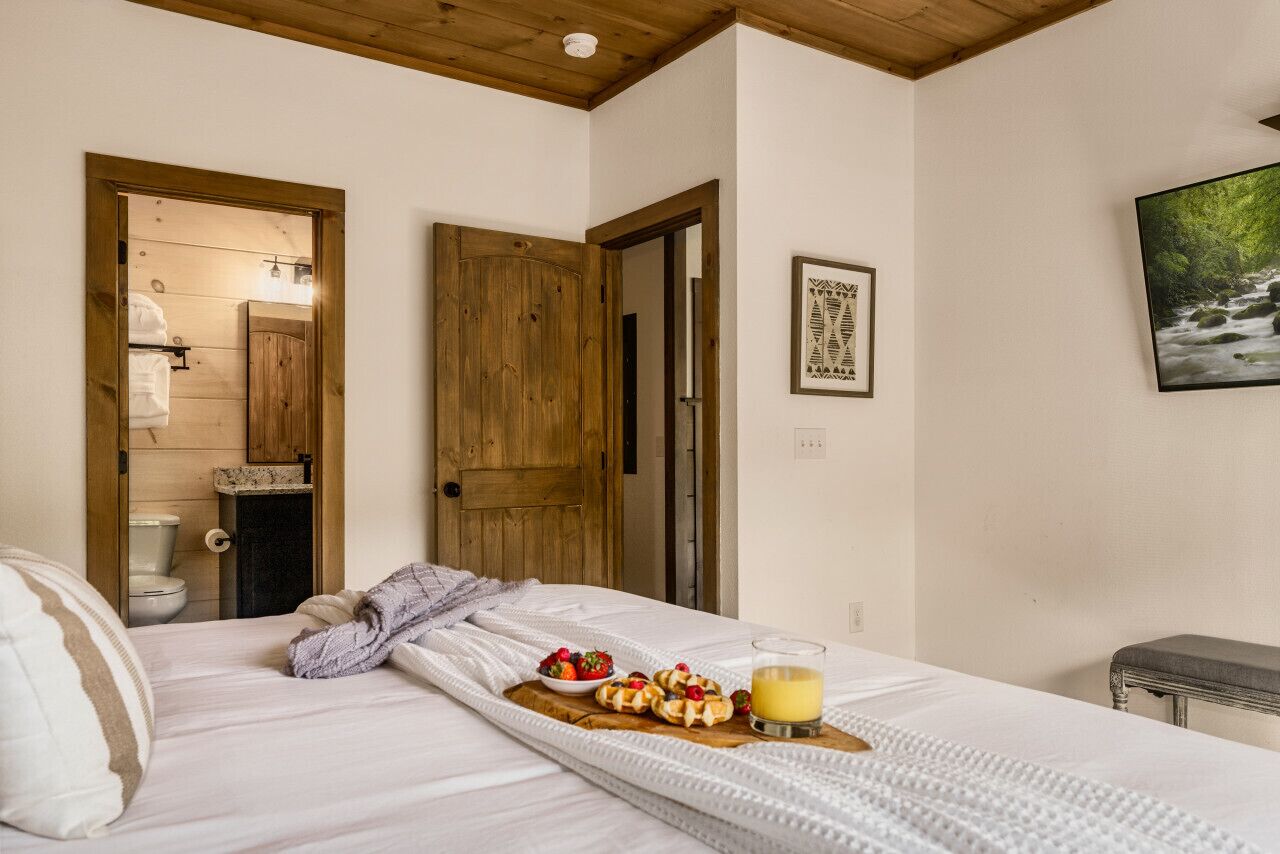 A bedroom with a bed, a breakfast tray with pastries and fruit, and a painting on the wall.
