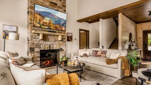 Un salon chaleureux avec une cheminée en pierre, un grand téléviseur à écran plat, un canapé confortable et une table basse avec des collations.