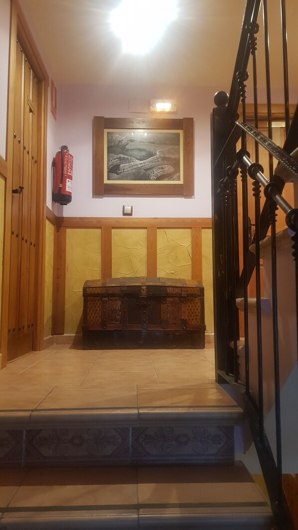A staircase with a metal railing, a fire extinguisher on the wall, and a framed landscape painting above the steps. - HTR-40/560 (Sebulcor)
