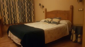 A neatly made bed with a patterned bedspread, a wooden headboard, and two bedside lamps. - HTR-40/560 (Sebulcor)