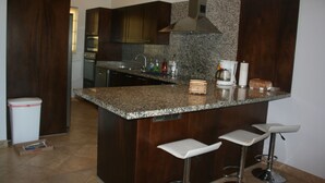A modern kitchen with dark wood cabinets, granite countertops, a stainless steel range hood, and a small bar area with stools. - GATED CONDO 2bd/2bth sleeps 5 Oceanview and Minutes from everything in Cabo! (Cabo San Lucas)