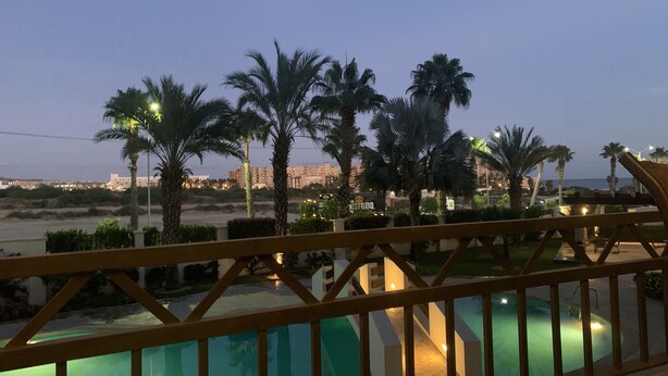 A pool area with a view of a cityscape and palm trees at dusk. - GATED CONDO 2bd/2bth sleeps 5 Oceanview and Minutes from everything in Cabo! (Cabo San Lucas)