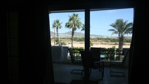 A room with a view of palm trees and a distant mountain. There is a chair and a table in the foreground. - GATED CONDO 2bd/2bth sleeps 5 Oceanview and Minutes from everything in Cabo! (Cabo San Lucas)