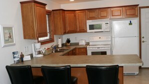 A kitchen with wooden cabinets, a microwave, a refrigerator, a stove, and a bar area with three chairs.