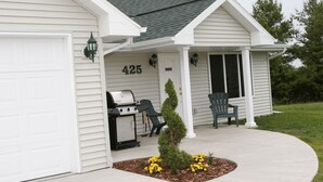 A house with a garage, a porch with a grill, and a small tree.