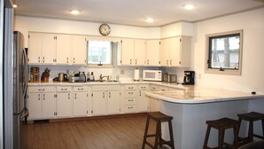 Una cocina con armarios blancos, microondas, cafetera y taburetes de madera.