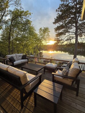 A wooden deck with outdoor furniture, a view of a lake, and trees in the background.
