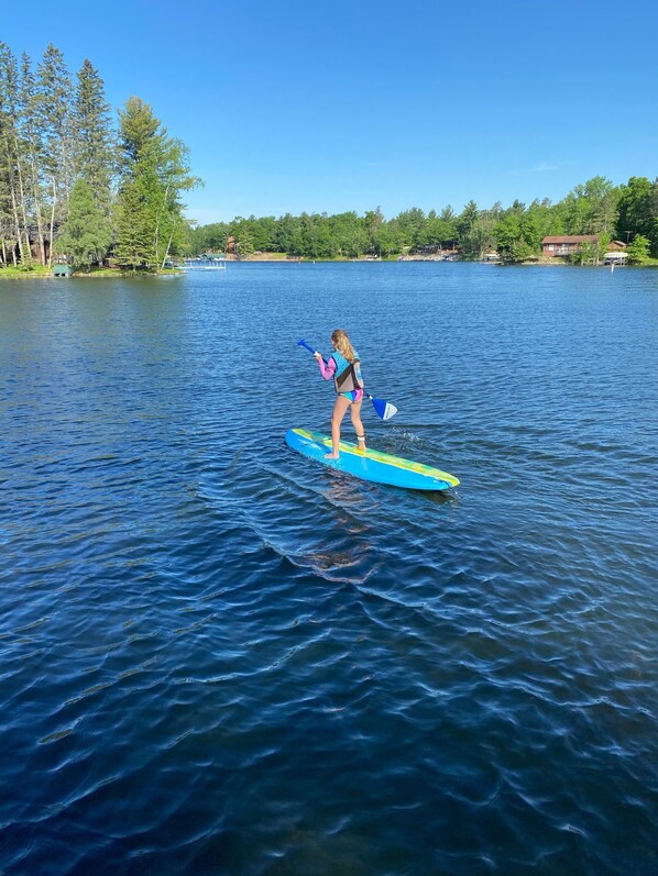 A person paddleboarding on a calm lake with trees and a house in the background.