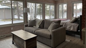 Una habitación acogedora con un ventanal grande, una mesa de madera y una cama con manta.