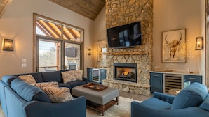 A cozy living room with a stone fireplace, a large flat-screen TV, and a comfortable seating area. - Birds Nest Retreat - Eagles Nest Village, hot tub, views, outdoor fireplace! (Banner Elk)